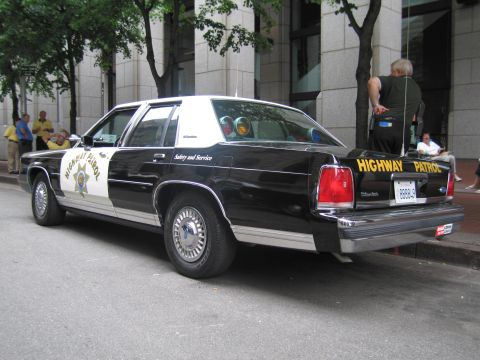 1991 Ford LTD Crown Victoria - Rear three-quarter of a black-and-white Highway Patrol sedan showing a star door shield and HIGHWAY PATROL across the trunk.