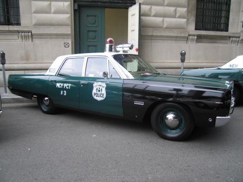 1991 Ford LTD Crown Victoria - restored green-and-black New York City police sedan lettered 'MCY PCT #3' with roof beacons sits curbside before a stone facade.
