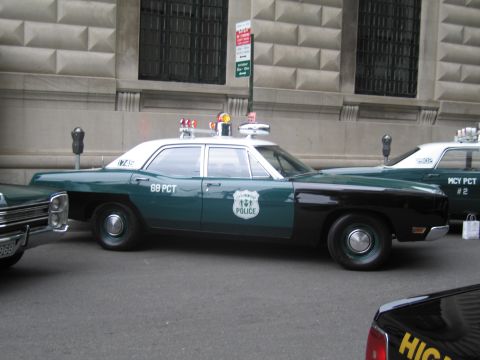 1991 Ford LTD Crown Victoria - side view of a restored green-and-black police sedan lettered '68 PCT' with roof beacons parked along a stone building.