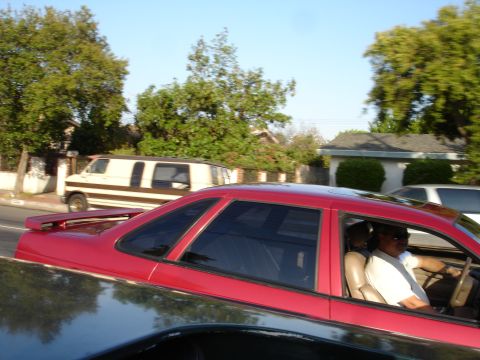 1993 Ford Taurus - A red coupe drives down a street with a van and another vehicle in the background.