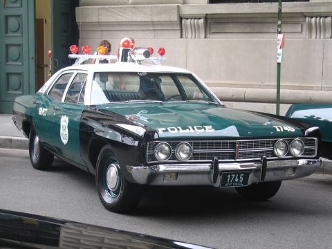 1991 Ford LTD Crown Victoria - front of a restored green-and-white police sedan lettered 'POLICE 1745' with red and clear roof beacons, parked beside a stone building.