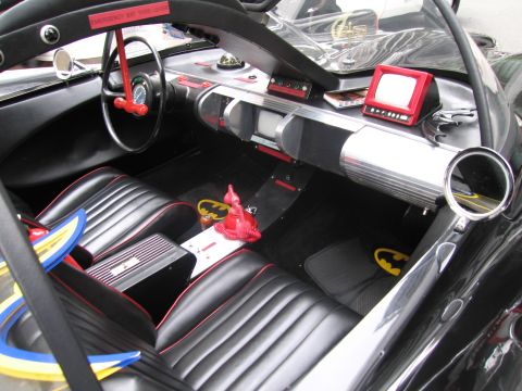 1991 Ford LTD Crown Victoria - black interior of a Batmobile replica with red pinstriping, a yellow bat-symbol floor mat, console screens and a red figurine.