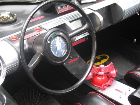 1991 Ford LTD Crown Victoria - cockpit of a Batmobile replica with a black steering wheel, central speedometer, red bat-phone and yellow bat-symbol floor mat.
