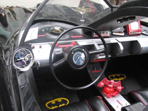 1991 Ford LTD Crown Victoria - driver area of a Batmobile replica showing the black wheel, gauge, silver finned console, red bat-phone and yellow bat-symbol floor mats.