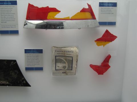 1991 Ford LTD Crown Victoria - museum exhibit case showing a battered red-and-amber taillight assembly, broken light fragments and a 'Crown Victoria' informational placar…