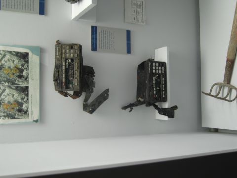 1991 Ford LTD Crown Victoria - Two charred, battered handheld radios mounted on white shelves in a museum case beside printed placards and aerial photographs.