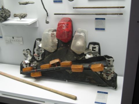 1991 Ford LTD Crown Victoria - heavily distorted black taillight panel with a red lens and orange reflectors rests on a white museum display surface near wall placards.