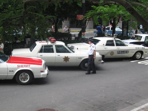 1991 Ford LTD Crown Victoria - white Sheriff sedan and a white Police sedan with roof beacons are parked while a uniformed officer stands between them on the street.