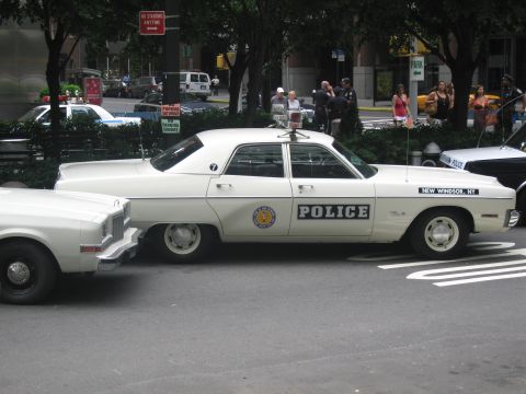 1991 Ford LTD Crown Victoria - white four-door Police sedan lettered New Windsor, NY, with a door shield emblem, is parked along a tree-lined city street with onlookers.