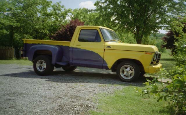 Yellow and purple Ford stepside pickup on a gravel driveway, side view