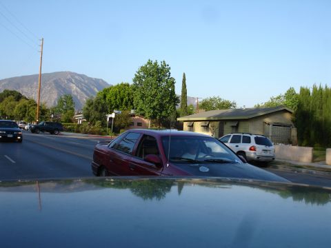 1993 Ford Taurus - A red 1993 Ford Taurus sedan is seen driving on a street, with a white SUV parked nearby.