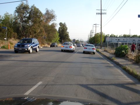1993 Ford Taurus - Multiple vehicles travel down a street lined with trees and utility poles under a clear sky.