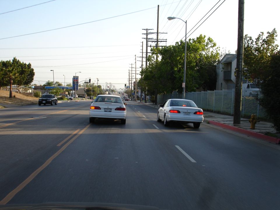 Two white sedans driving on a road, one in front of the other