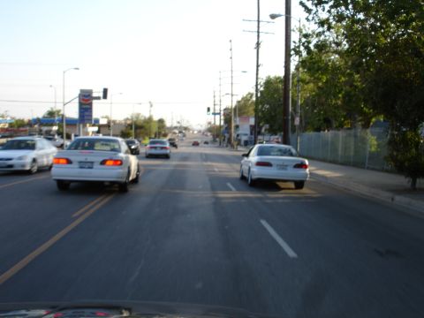 1993 Ford Taurus - A white sedan travels down a multi-lane road, passing a gas station under a bright sky.