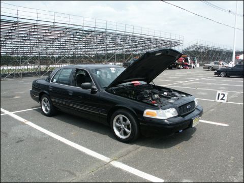 2001 Mercury Grand Marquis - Black sedan with hood open, parked in a lot with bleachers in the background.