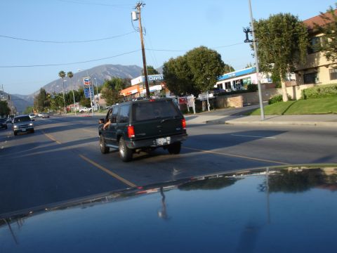 1993 Ford Taurus - A dark green SUV with a roof rack drives down a suburban street on a clear day.