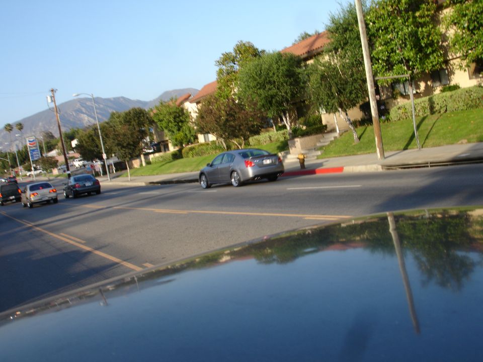 Silver sedan driving on a street with apartment buildings and mountains in the background