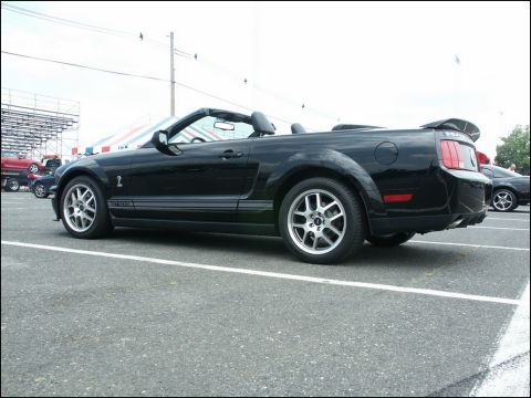 2001 Mercury Grand Marquis - A black convertible Mustang is parked in a lot, with bleachers and another car visible in the background.