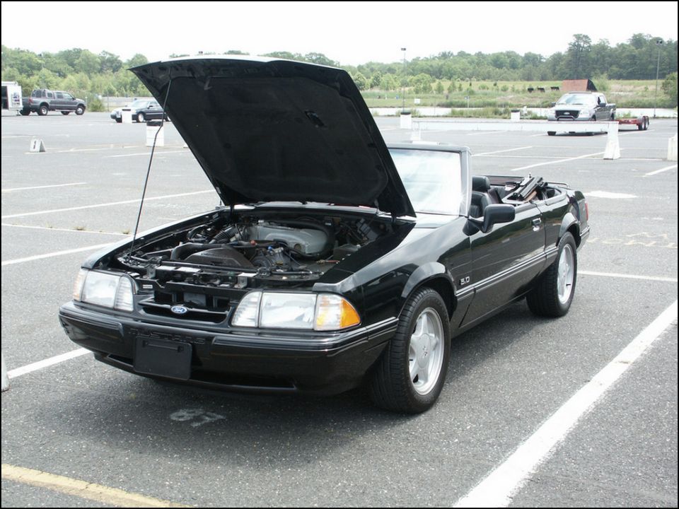 Black convertible with hood open, showing engine. "5.0" badge visible on fender