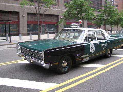 1991 Ford LTD Crown Victoria - dark green-and-white classic police sedan with a roof beacon, lettered MCY PCT #3, parks at a city curb beside another patrol car.