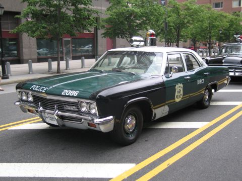1991 Ford LTD Crown Victoria - green-and-white POLICE sedan numbered 2086, marked 18 PCT, sits on a city street with a roof beacon and another classic patrol car behind.
