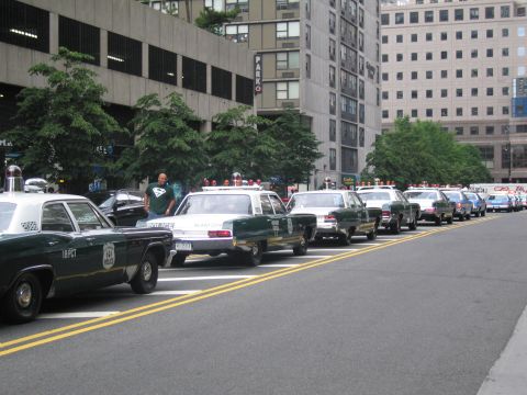 1991 Ford LTD Crown Victoria - long line of vintage police cars, including green-and-white and black-and-white sedans, is parked along a city street as a man stands among…