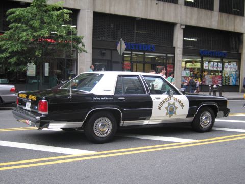 1991 Ford LTD Crown Victoria - black-and-white Highway Patrol sedan marked Safety and Service is parked at a city curb in front of a Gristedes storefront, seen from the r…