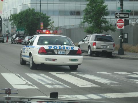 1991 Ford LTD Crown Victoria - white NYPD police car marked 1215 with red roof lights sits at a crosswalk near a silver SUV and One Way signs.