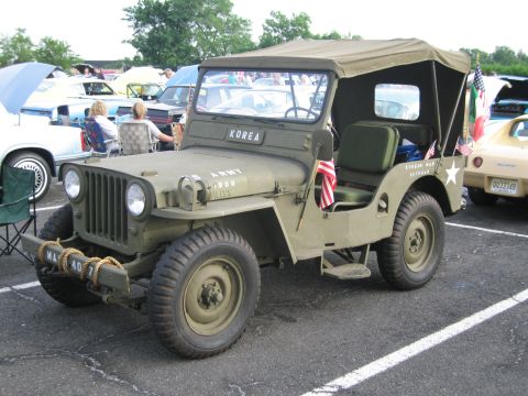 1991 Ford LTD Crown Victoria - olive-drab military Jeep lettered KOREA with a small American flag sits in a parking lot at an outdoor vehicle show.