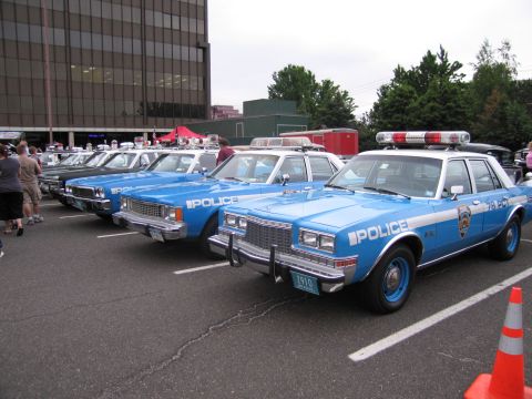 1991 Ford LTD Crown Victoria - lineup of restored blue-and-white NYPD police sedans parked diagonally at an outdoor car show, marked POLICE.