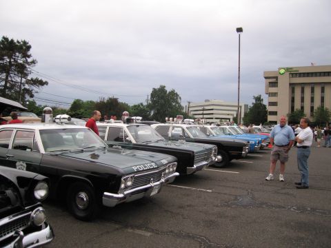 1991 Ford LTD Crown Victoria - long row of classic black-and-white police sedans parked side by side at an outdoor car show as visitors look on.