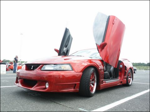 2001 Mercury Grand Marquis - A red Ford Mustang with custom doors is displayed at an outdoor car show.