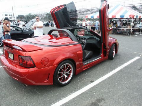 2001 Mercury Grand Marquis - A red convertible sports car with its doors open, parked at an outdoor event.