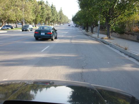 1993 Ford Taurus - A green sedan is seen driving down a tree-lined street, with other vehicles also visible on the road.
