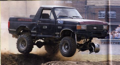 1981 Ford Bronco - This black 1981 Ford Bronco, identified by its "BRONCORACING" decal, is captured mid-air during an apparent off-road event.