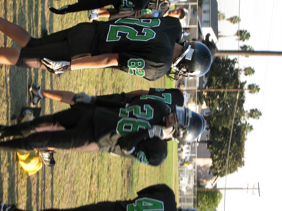 Football players in black and green uniforms on a grassy field