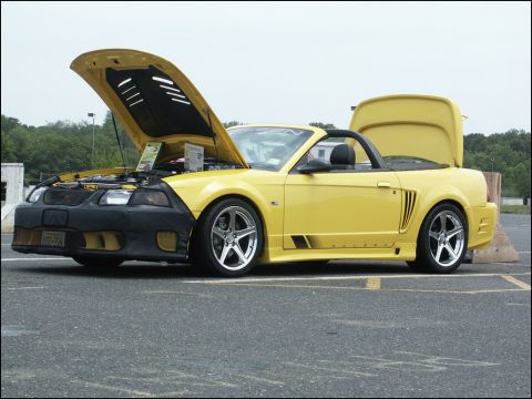 2001 Mercury Grand Marquis - A yellow convertible is displayed with its hood and trunk open, revealing the engine and interior at a car show.