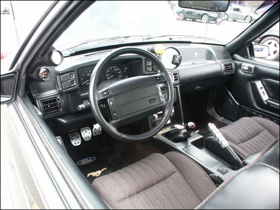 Interior view of a car with aftermarket gauges and a Ford logo on the floor mat