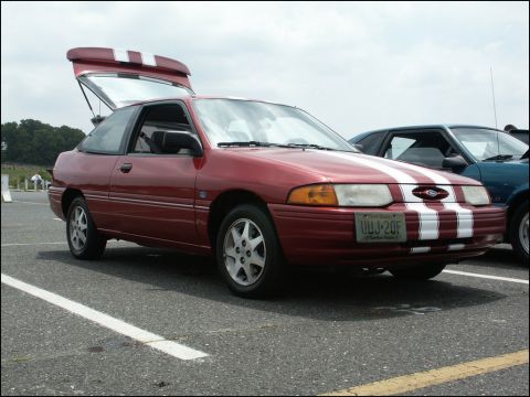 2001 Mercury Grand Marquis - A red hatchback with racing stripes is parked in a lot, with its trunk open.