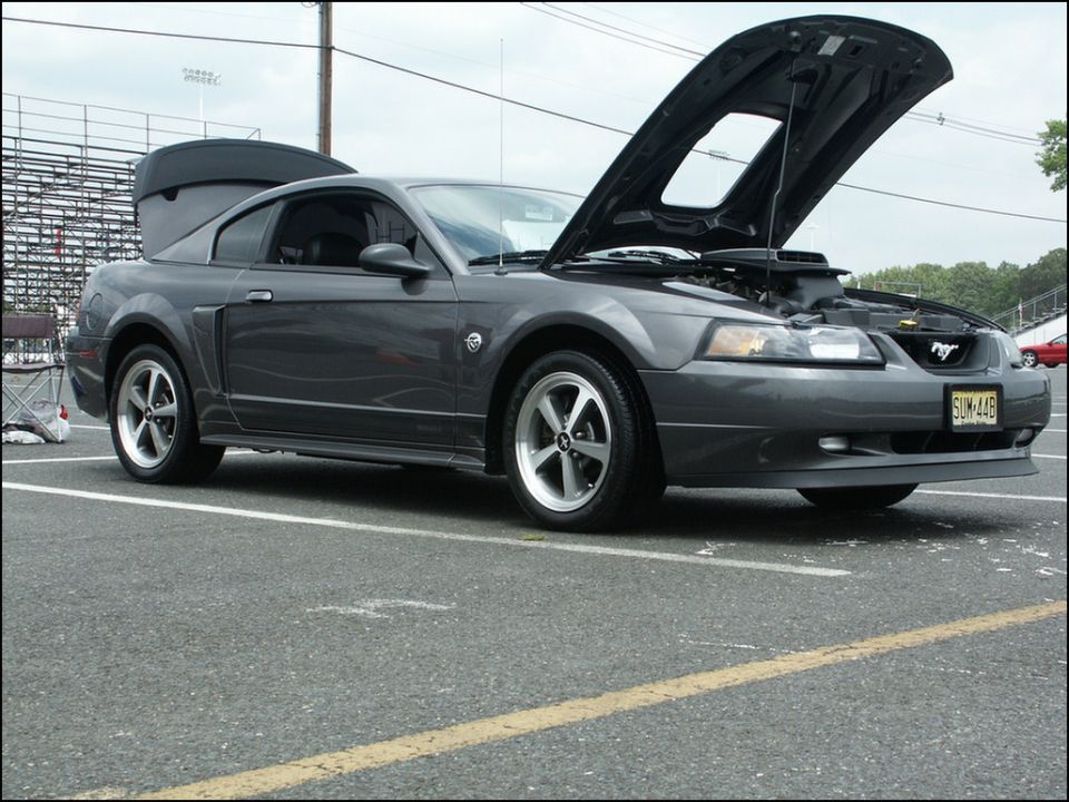 Dark gray Ford Mustang with hood and trunk open, parked on asphalt