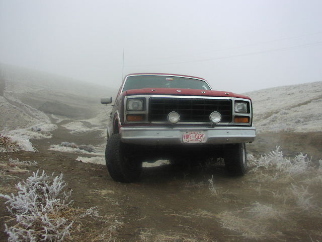 Front view of a red pickup truck with a black grille and "FIRE DEPT" plate, parked on a dirt road in foggy conditions