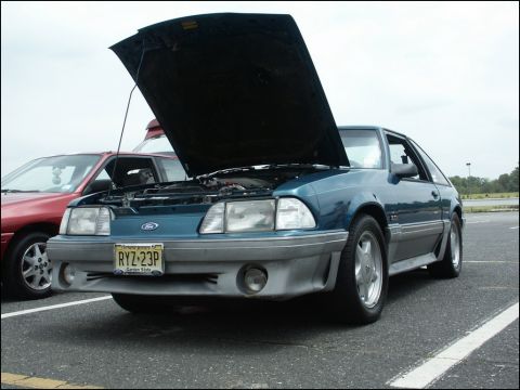 2001 Mercury Grand Marquis - Teal Ford Mustang, hood up, parked at an outdoor event. Another car is visible to the left.
