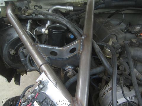 1990 Ford Bronco - Detail of a welded steel tube and triangular gusset plate routed through an engine bay among hoses, wiring, and components.