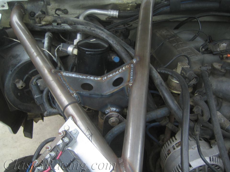 Close-up of welded tubular cage tube and gusset plate routed through an engine bay