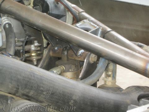 1990 Ford Bronco - Close-up of a fuel-system component labeled Racing and a tubular cage bar surrounded by engine hoses and fittings.