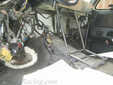 1990 Ford Bronco - Gutted vehicle interior showing exposed wiring harnesses, bare floor pan, and welded tubular roll-cage bars on the passenger side.