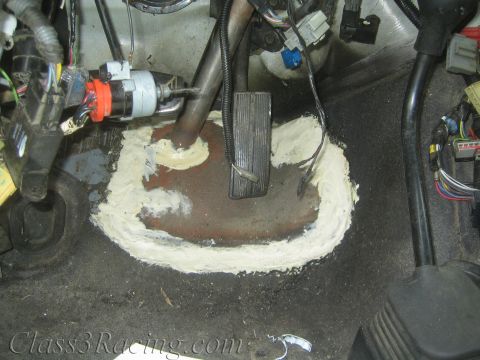 1990 Ford Bronco - Looking down at a vehicle floor opening ringed with expanding foam, with routed hoses and bundled wiring harnesses around it.