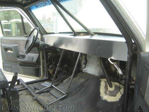 1990 Ford Bronco - Stripped truck cab interior with a tubular cage, fabricated sheet-metal dash panel, and a gray door panel, viewed from passenger side.