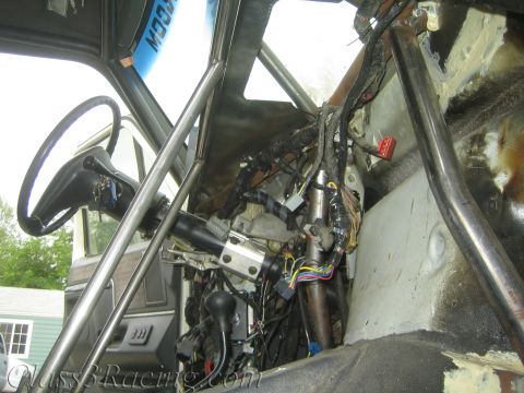 1990 Ford Bronco - Bare vehicle interior with steering column, tubular cage bars, and a dense bundle of exposed wiring against bare sheet metal.