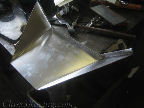 1990 Ford Bronco - freshly folded and welded bare sheet-metal part sits on a steel workbench beside hammers and hand tools in a shop.